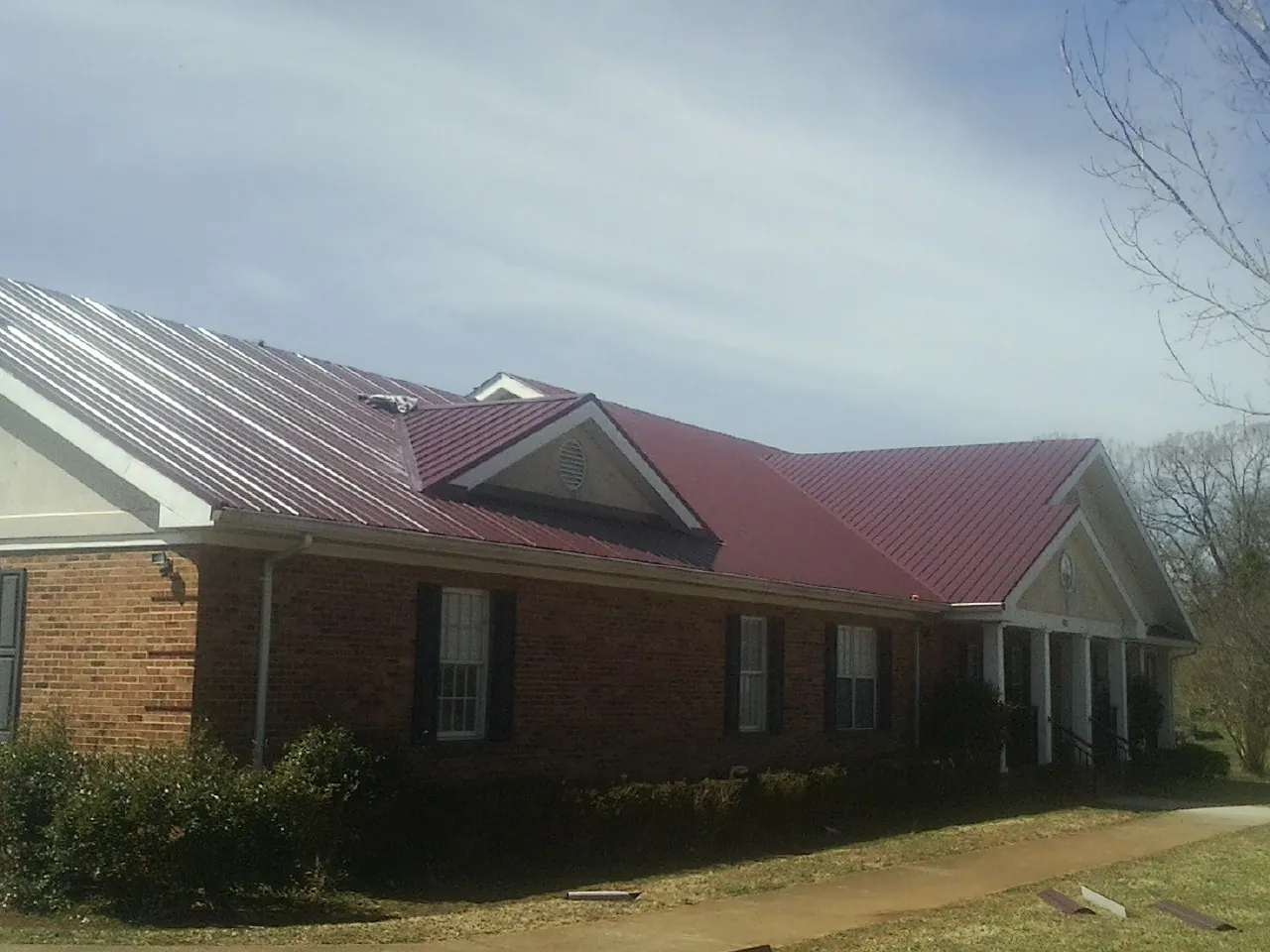 Red metal roof with gabled entries on a long brick building, from a Hail Damage Roof Repair job in Cedarville