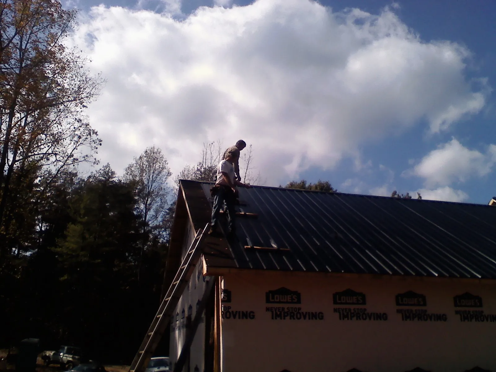 Roofer fastening dark metal panels high against a cloudy sky, from a Roof Inspection job in Cedarville